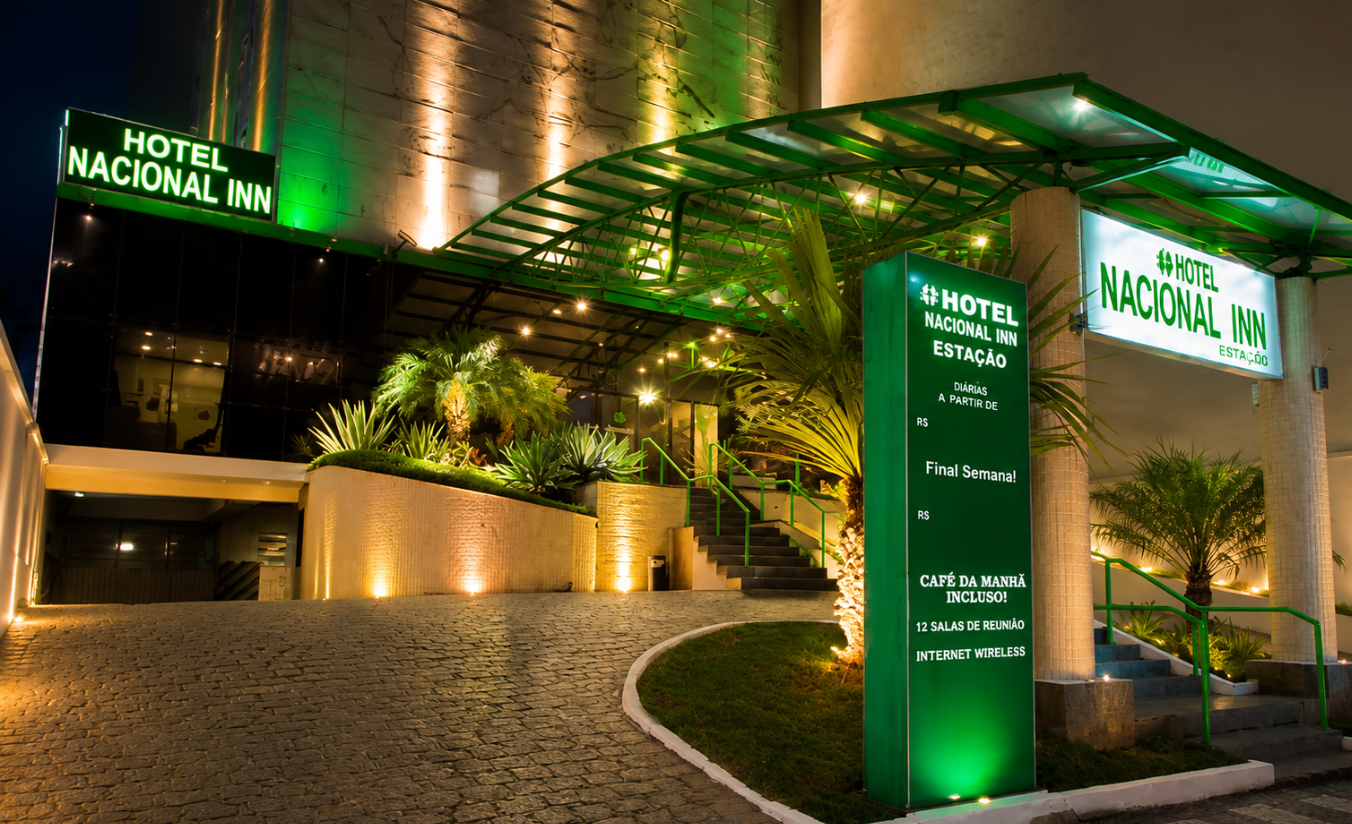 Fachada iluminada de hotel moderno em Curitiba à noite com entrada acolhedora e árvores ao redor