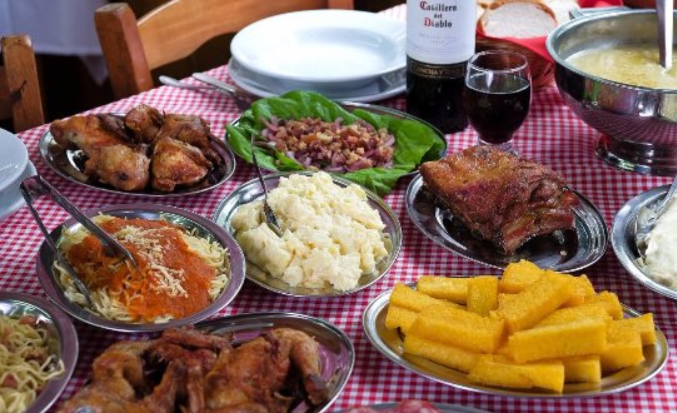 Mesa farta em cantina tradicional de Santa Felicidade com massas, frango ao molho e vinho tinto