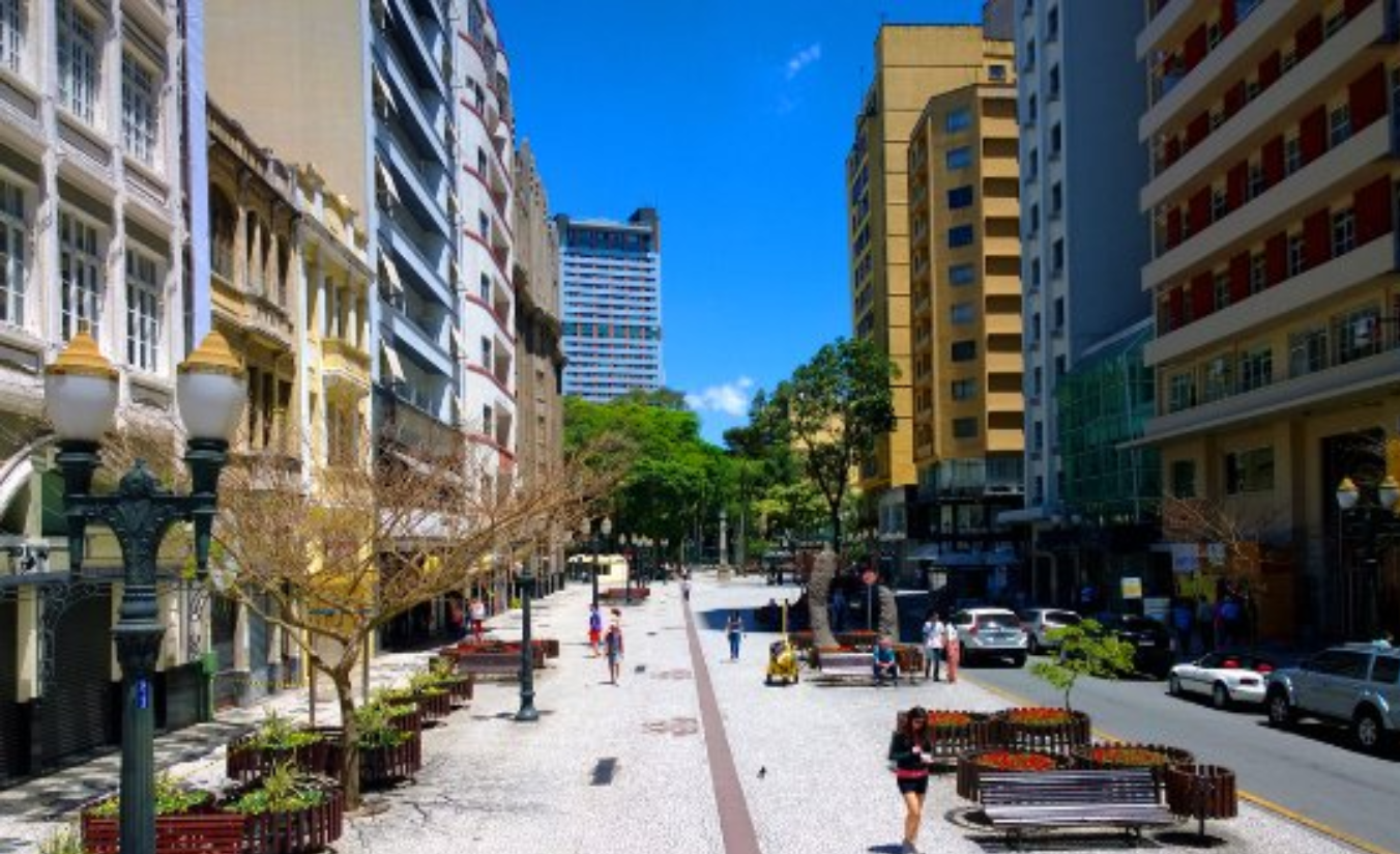 Rua XV de Novembro em Curitiba com calçadão de petit-pavé, flores coloridas e pedestres ao entardecer