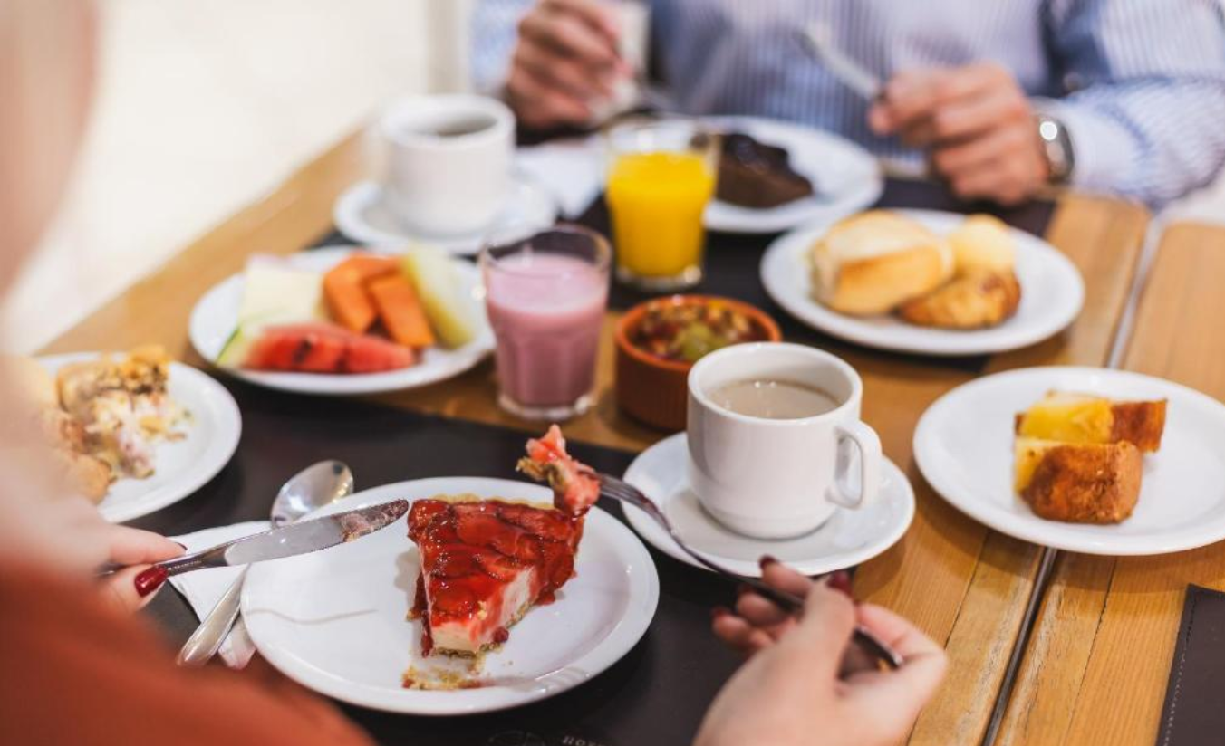 Café da manhã completo servido no hotel, com pães, frutas, bebidas e opções variadas para os hóspedes